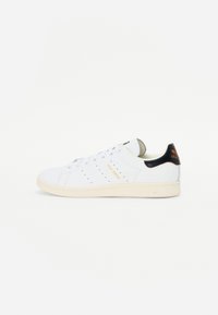 Hvid læder sneakers med perforerede detaljer, brune accenter og gummisål. Udstyret med "Stan Smith" branding i guld. Rent design med polstret krave.