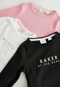Drie geribbelde longsleeves in het roze, wit en zwart, met de tekst "BAKER BY TED BAKER" in het goud gedrukt op de voorkant.
