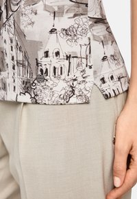 Short-sleeve top with a beige and black architectural print, featuring a rounded hem and side slit. Paired with light beige trousers.