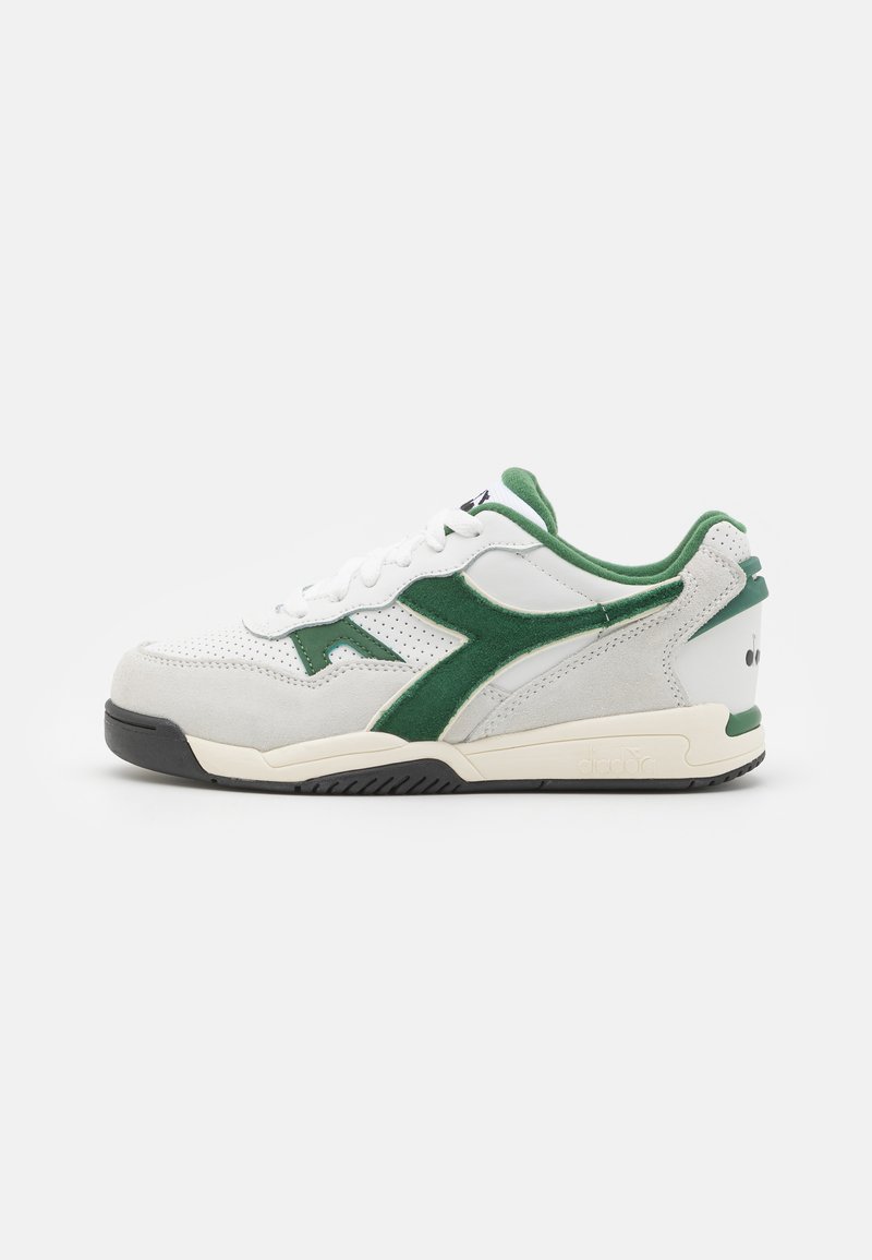 White sneaker with green suede accents, perforated leather, black rubber sole, and padded collar. Features a logo on the heel and gray midsole.