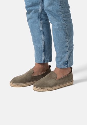 Lichtbruine suède instapschoenen met geweven jute zolen, met een gladde textuur en uitsparingen aan de zijkanten, gedragen met een lichte spijkerbroek.