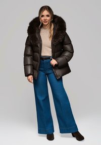 Giacca a vento marrone con cappuccio in finta pelliccia, abbinata a jeans a gamba larga blu a vita alta e stivaletti neri. Maglietta beige semplice sotto.