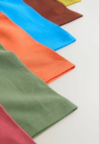 Sex stygn av tyg i olika färger: grön, orange, rosa, blå, brun och gul. Slät textur med synliga sömmar längs kanterna.