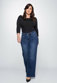 Zwarte langslavende bodysuit gecombineerd met hoge taille, wijde donkerblauwe jeans. Soepele stof en klassieke denimafwerking. Zwarte hakken maken de look af.