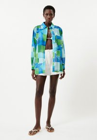 Mehrfarbiges Hemd in Blau- und Grüntönen, mit einem knopfbeschichteten Design, Kragen und langen Ärmeln, getragen mit weißen Shorts.