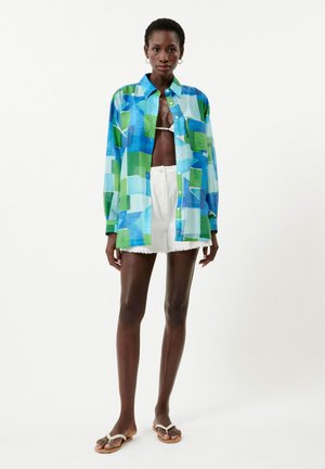 Multikleurig shirt in tinten blauw en groen, met een knoopsluiting, kraag en lange mouwen, gedragen met witte shorts.