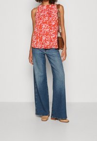 Top senza maniche a righe rosse e rosa con scollo arricciato, abbinato a jeans blu con gamba ampia e scarpe con tacco quadrato marrone chiaro.