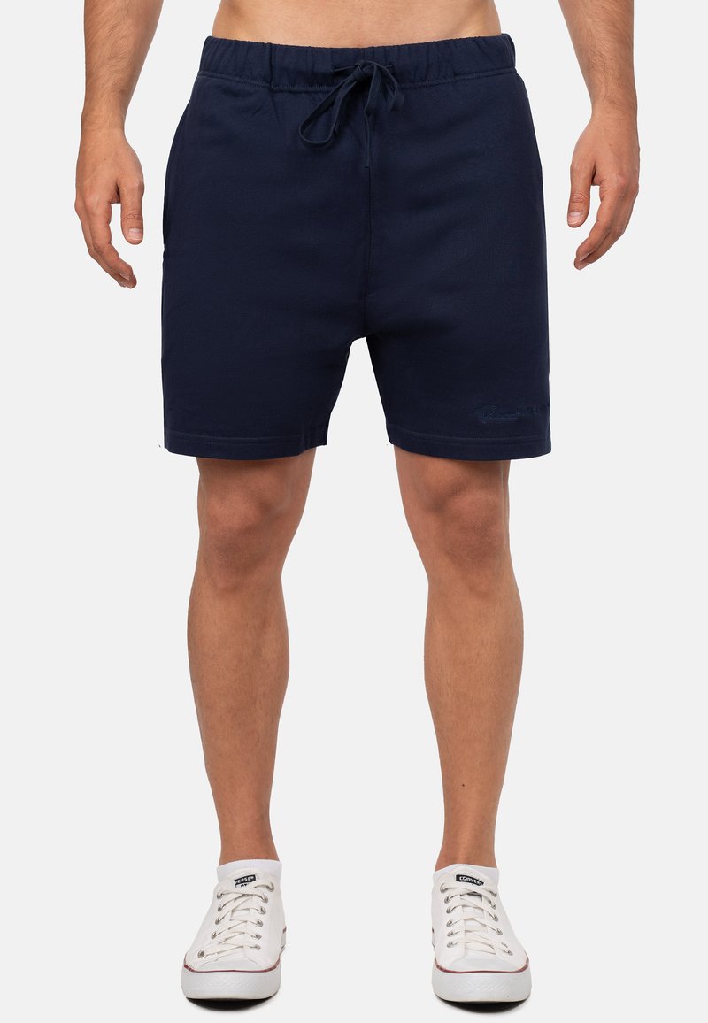 Pantaloni da bagno blu navy con vita elastica e cordino. Presentano tasche laterali e un piccolo logo ricamato sulla coscia sinistra.