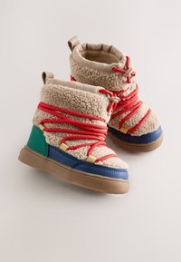 Stivali invernali beige da bambini con fodera in pile, lacci rossi, puntali blu, toppe verdi sul tallone e suole in gomma marrone su uno sfondo semplice.