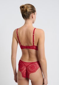 Conjunto de lencería de encaje rojo que incluye un sujetador con tirantes ajustables y una braga a juego con bordados florales y detalles transparentes.