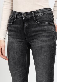 Schwarze Denim-Jeans im Slim-Fit, mit Kontrastnähten, Fünf-Taschen-Design und einem Markenetikett auf der vorderen Tasche.