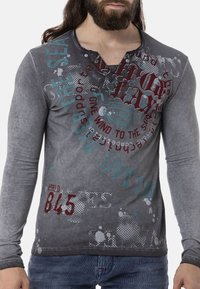 Langärmliges graues T-Shirt mit strukturiertem Finish, grafischen Drucken in Rot und Teal, abgerundetem Kragen und Knopf-Akzenten.