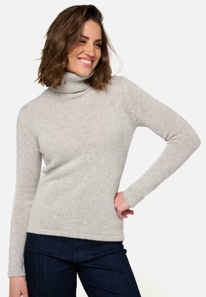 Pull en col roulé gris clair avec une texture côtelée, une coupe ajustée et des manches longues, associé à un jean bleu foncé.