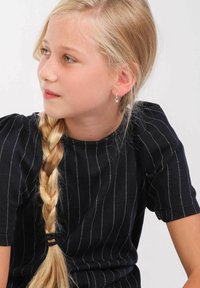 Schwarz gestreifte Bluse mit Puffärmeln, getragen von einem Mädchen mit geflochtenem Haar. Silberne Creolen sind sichtbar. Einfaches, klares Design.