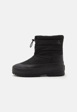 Botte isolante noire mi-mollet avec semelle épaisse et cordon ajustable en haut, avec un logo discret "cK" près de la cheville.