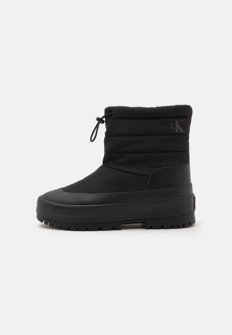 Botte isolante noire mi-mollet avec semelle épaisse et cordon ajustable en haut, avec un logo discret "cK" près de la cheville.