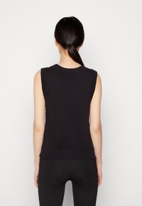 Svart ärmlös trikåtopp med ribbad halsringning och nederkant. Slät textur, figurnära silhuett och minimalistisk design. Inga synliga utsmyckningar.