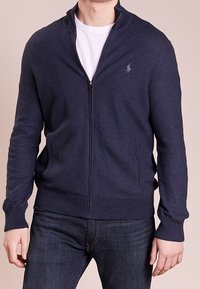 Marinblå zip-up sweater med en texturerad stickning, utrustad med hög krage, subtil logotyp på bröstet och två sidofickor.