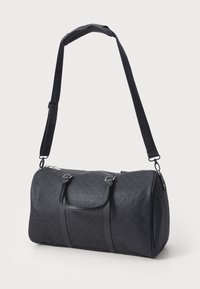 Sort duffeltaske lavet af tekstureret materiale med lynlås, to bærehåndtag og en justerbar skulderrem. Har diskrete logomønstre.