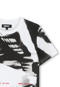 Witte katoenen t-shirt met een zwart-wit abstract patroon, ronde halslijn en de tekst "DKNY EST. 1989" in het rood langs de onderkant.