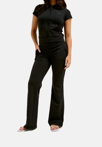 Zwarte actieve set met een kort mouw zip-up top en flare broeken, beide gemaakt van een glad, rekbaar materiaal, met zijzakken.