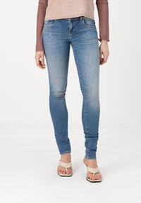 Modré skinny džíny vyrobené z denimu, s vybledlým efektem, pěti kapsami a jemnými švy, doplněné o ploché sandály.