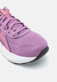 Chaussure de sport violette avec un upper en maille respirante, des motifs texturés, des accents roses, une semelle intermédiaire blanche épaisse et une semelle extérieure en caoutchouc noire.