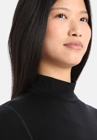 Sort turtleneck-top lavet af glat stof, med høj hals og tætsiddende design, med minimale syninger synlige.