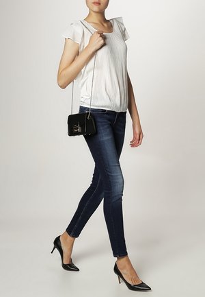 Ljus, plisserad vit blus med korta svängande ärmar, mörka skinny jeans och svarta lackade högklackade skor. Liten svart axelremsväska.