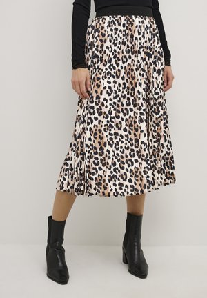 Femme portant une jupe midi plissée avec un imprimé léopard marron, noir et blanc et des bottines noires à talons.