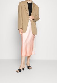 Blazer beige de gran tamaño, top negro ajustado y falda midi satinada en tono rosa con cordón. Unos mules abiertos negros completan el atuendo.