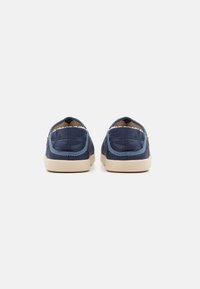 Navy quilted slip-on shoes with a textile upper, light beige rubber sole, and a soft lining, featuring stitched detailing around the opening.