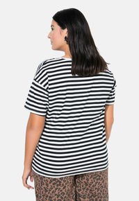 Camiseta de rayas negras y blancas con mangas cortas y un corte relajado. La tela parece suave, complementada por pantalones de leopardo en contraste.