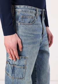 Lyst blå denim jeans med en afslappet pasform, der har en lomme på låret, kobberfarvet syning og et vævet mærke nær lommen.