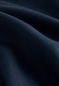 Ciemnoniebieska tkanina o miękkiej, teksturowanej powierzchni, z delikatnymi detalami dzianinowymi i gładkimi, płynącymi fałdami.