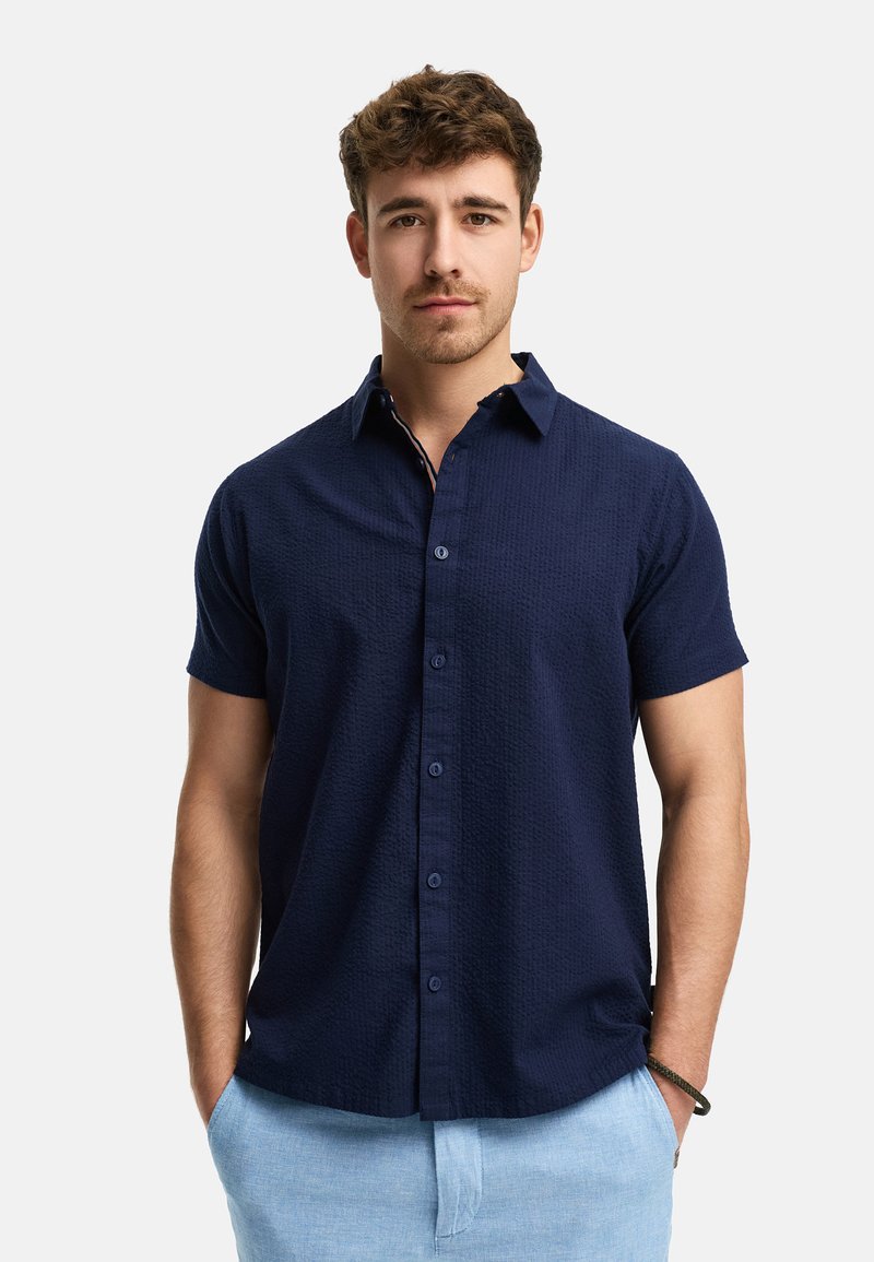 Camisa de manga corta de color navy, con tejido texturizado, cierre de botones en la parte delantera, cuello y botones a juego, combinada con pantalones de color azul claro.