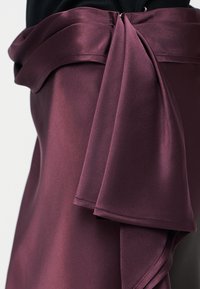 Prim plan cu o fustă din satin neted, de culoare mov închis, cu o centură lată din aceeași stofă legată într-un nod lejer în talie, purtată cu un top negru.