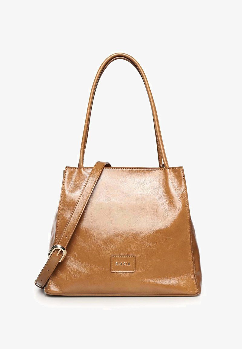 Bolso tote de cuero marrón medio con asas largas y una correa de hombro ajustable, con un pequeño parche rectangular de la marca en el frente.