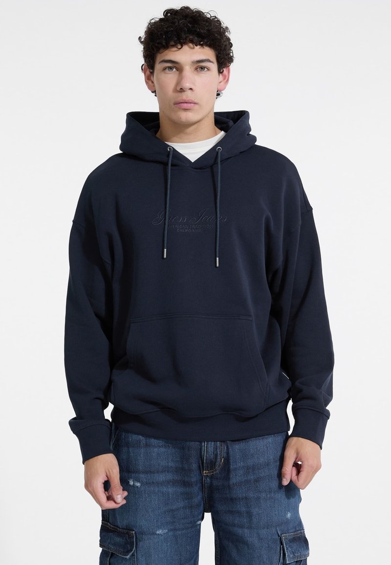 Sudadera con capucha de color azul marino en mezcla de algodón, con bolsillo frontal, cordón y logo en relieve. Corte holgado con puños de canalé.