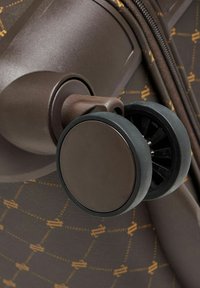 Maleta de viaje marrón con un acabado elegante, que presenta una rueda negra circular, un patrón grabado y un detalle de cremallera suave.