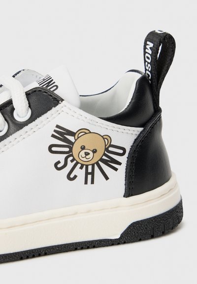 Sorte og hvite sneakers med et bjørne-motiv og "MOSCHINO" merkevare, med en glatt skinnøvre og teksturert gummisåle.