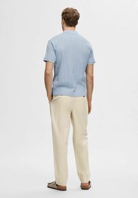 Svijetloplava rebrasta polo majica kratkih rukava, krem hlače i smeđe cipele na vezivanje, prikazane sa stražnje strane na jednobojnoj pozadini.