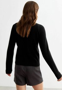 Maglione nero con texture e maniche lunghe, caratterizzato da un colletto rotondo. Il capo è abbinato a pantaloni corti a righe.