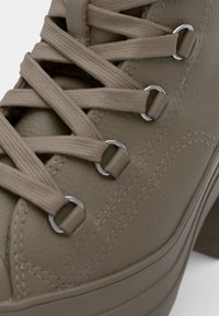 Beige high-top sneaker featuring textured leather, flat laces, metallic eyelets, and a sturdy sole with visible stitching details.