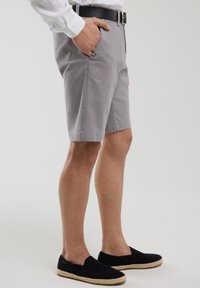 Shorts en coton gris avec poches latérales, coupe droite et ourlets repliés. Associés à des chaussures noires à enfiler avec une semelle en jute.