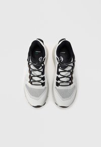 Paar von weißen und schwarzen Sportlaufschuhen mit Mesh-Obermaterial und schwarzen Schnürsenkeln auf einem hellgrauen Hintergrund.