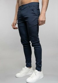 Tmavě modré kalhoty slim fit z texturované látky, s předními kapsami a zapínáním na knoflíky. Doplněné bílými teniskami.