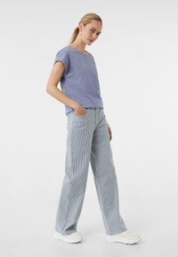 Helllila Kurzarm-T-Shirt mit Rundhalsausschnitt, kombiniert mit gestreiften, weit geschnittenen Hosen in Blau und Weiß. Beide Teile haben einen lässigen Schnitt.