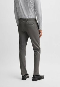 Pantalon gris pour homme, coupe ajustée, fabriqué en tissu lisse. Dispose de poches arrière et d'un logo de marque discret au-dessus de la poche droite.