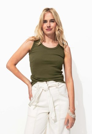 Débardeur côtelé vert olive avec un col rond, associé à un pantalon blanc taille haute avec une ceinture nouée et des détails de couture visibles.